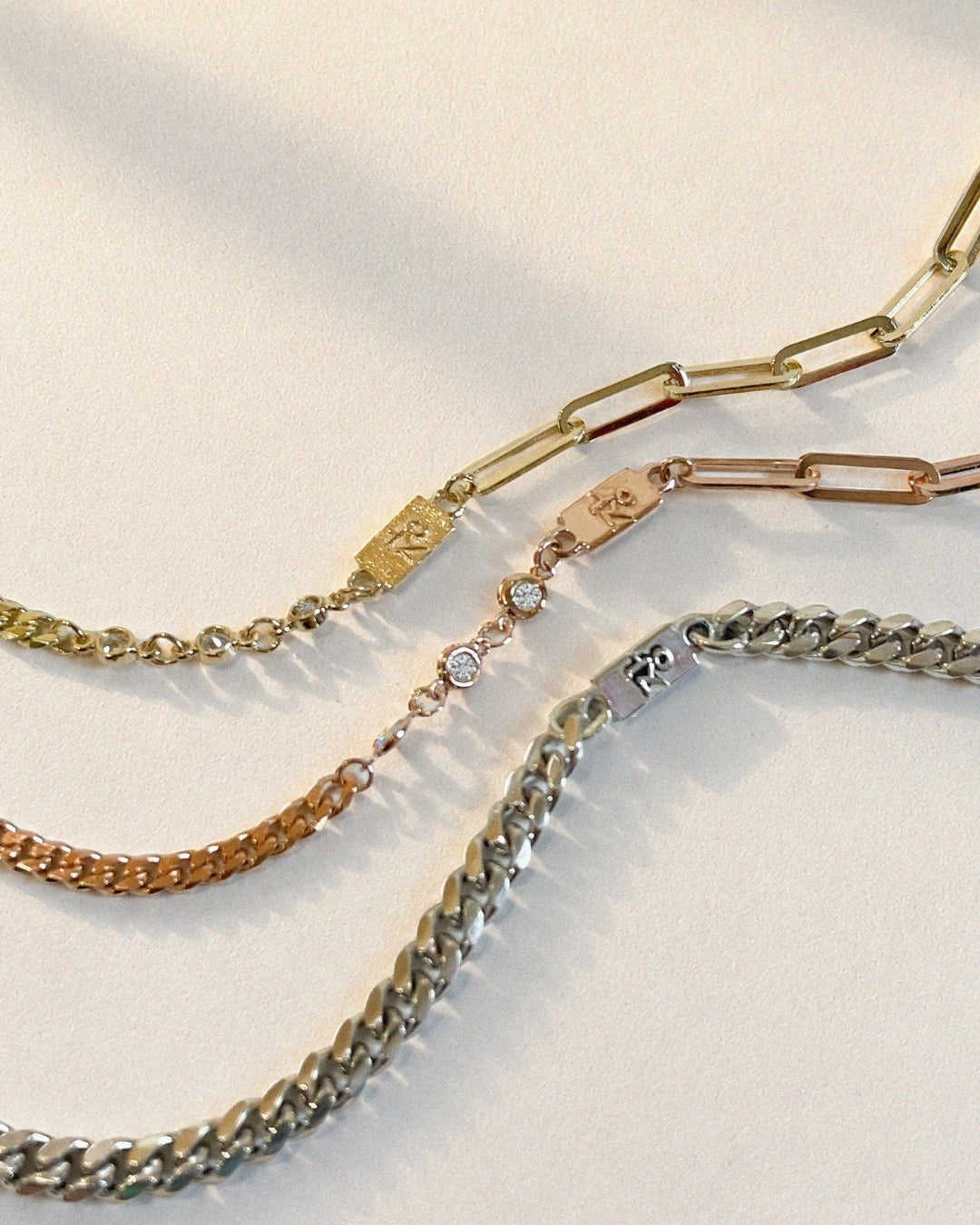 Three custom bracelets arranged on a softly lit white surface. The set includes a yellow gold mixed-link bracelet with a rectangular Korean nameplate, a rose gold bracelet with bezel-set round diamonds and a matching nameplate, and a sterling silver curb chain bracelet. Each bracelet features the raised Korean character "장," symbolizing a shared family connection while reflecting each wearer's individual style.