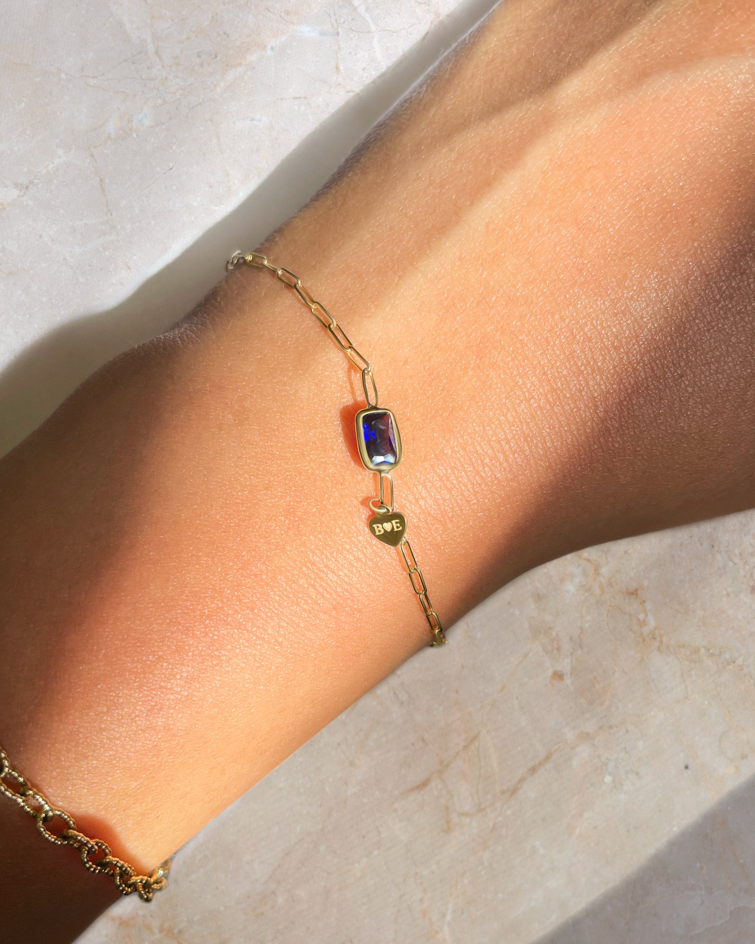 Gold bracelet with a blue gemstone on a wrist against a neutral background