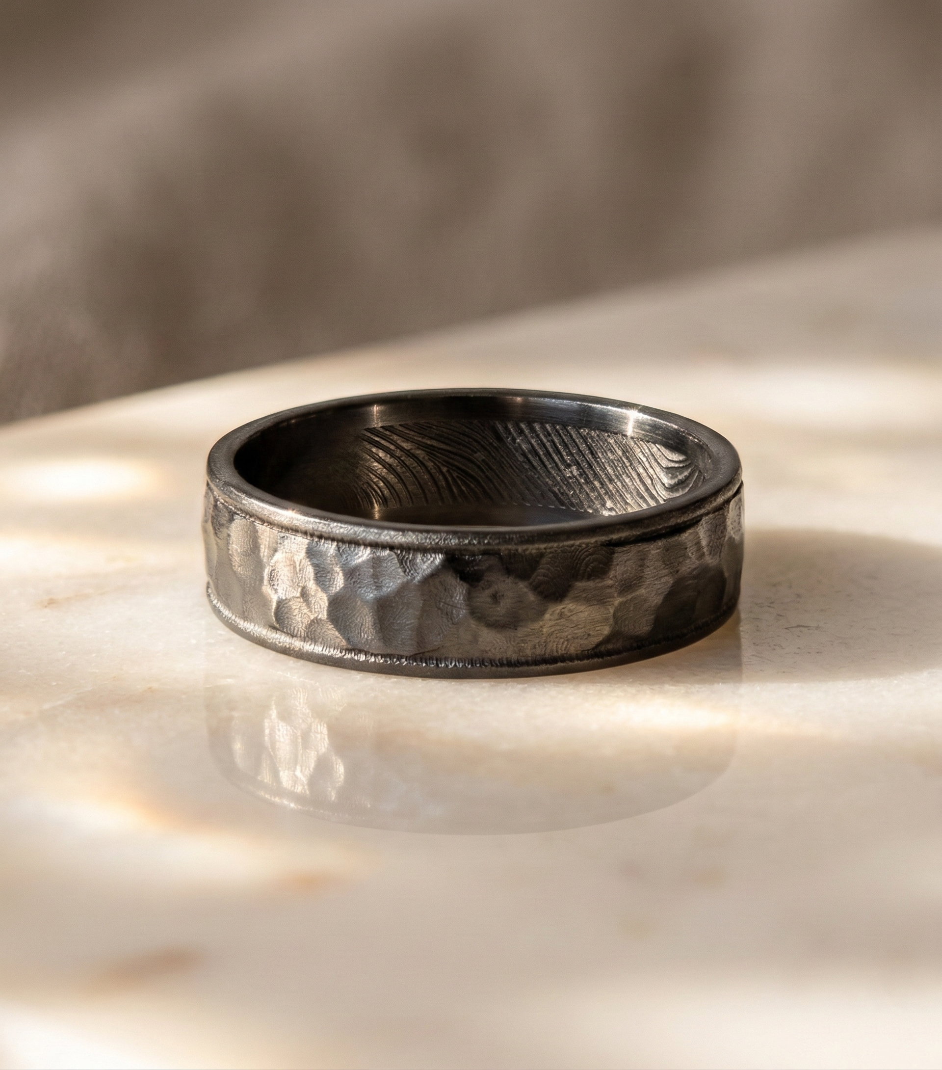 Textured black ring with a fingerprint embedded on the interior band, on a light surface with a blurred background