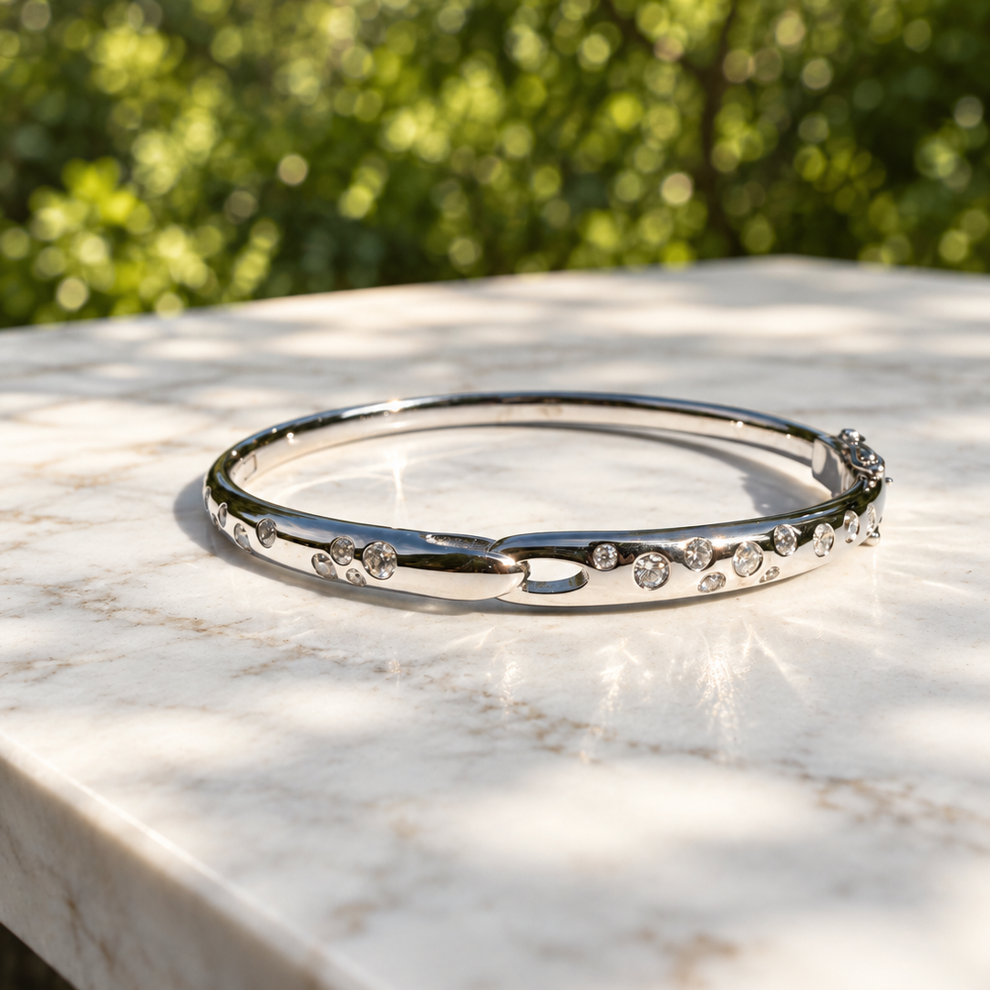 Polished silver hinged bangle bracelet set with scattered round diamonds, photographed outdoors on a white marble surface in direct sunlight.