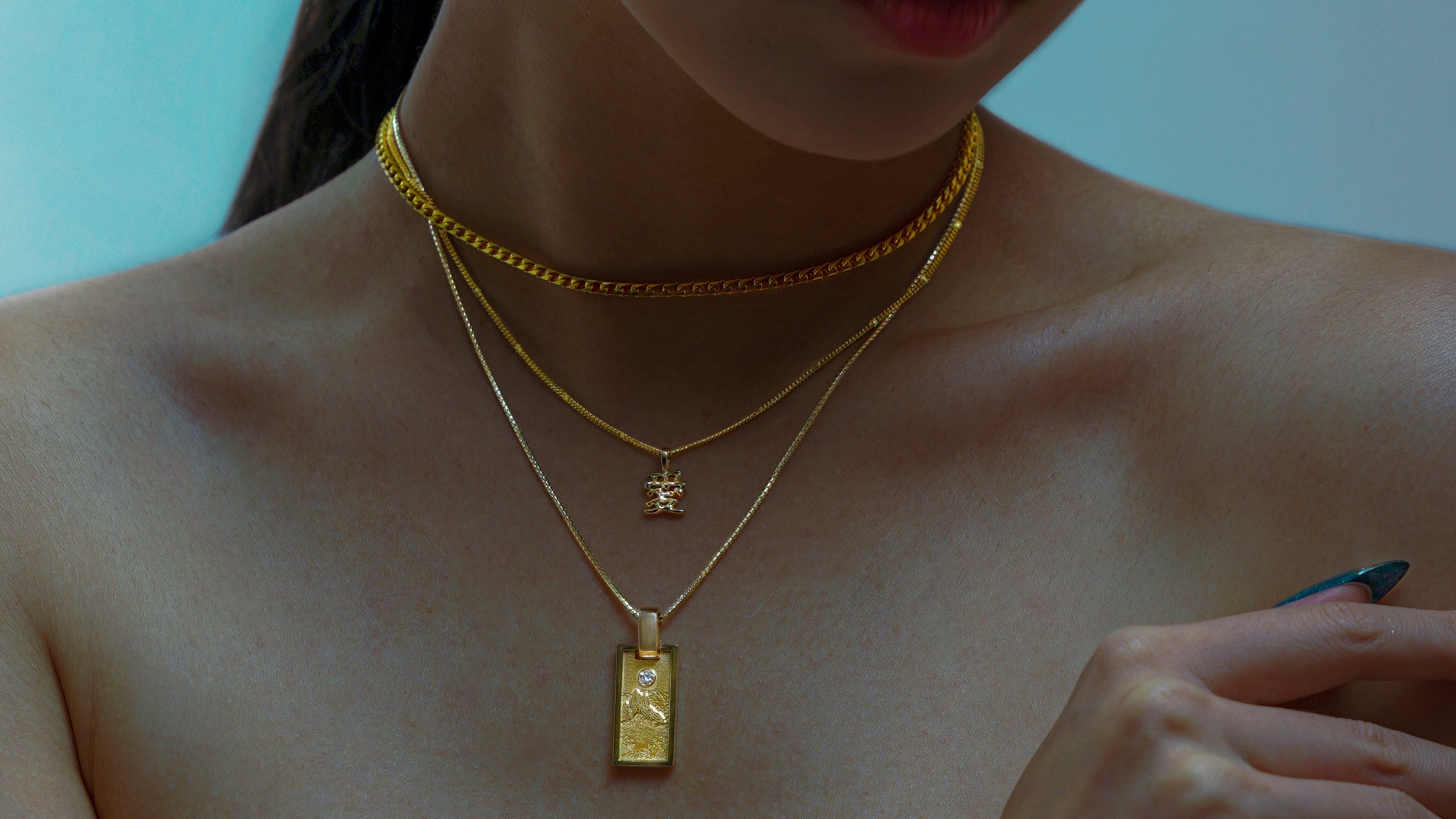 Close-up of a person wearing multiple NUNCHI gold necklaces with pendants.