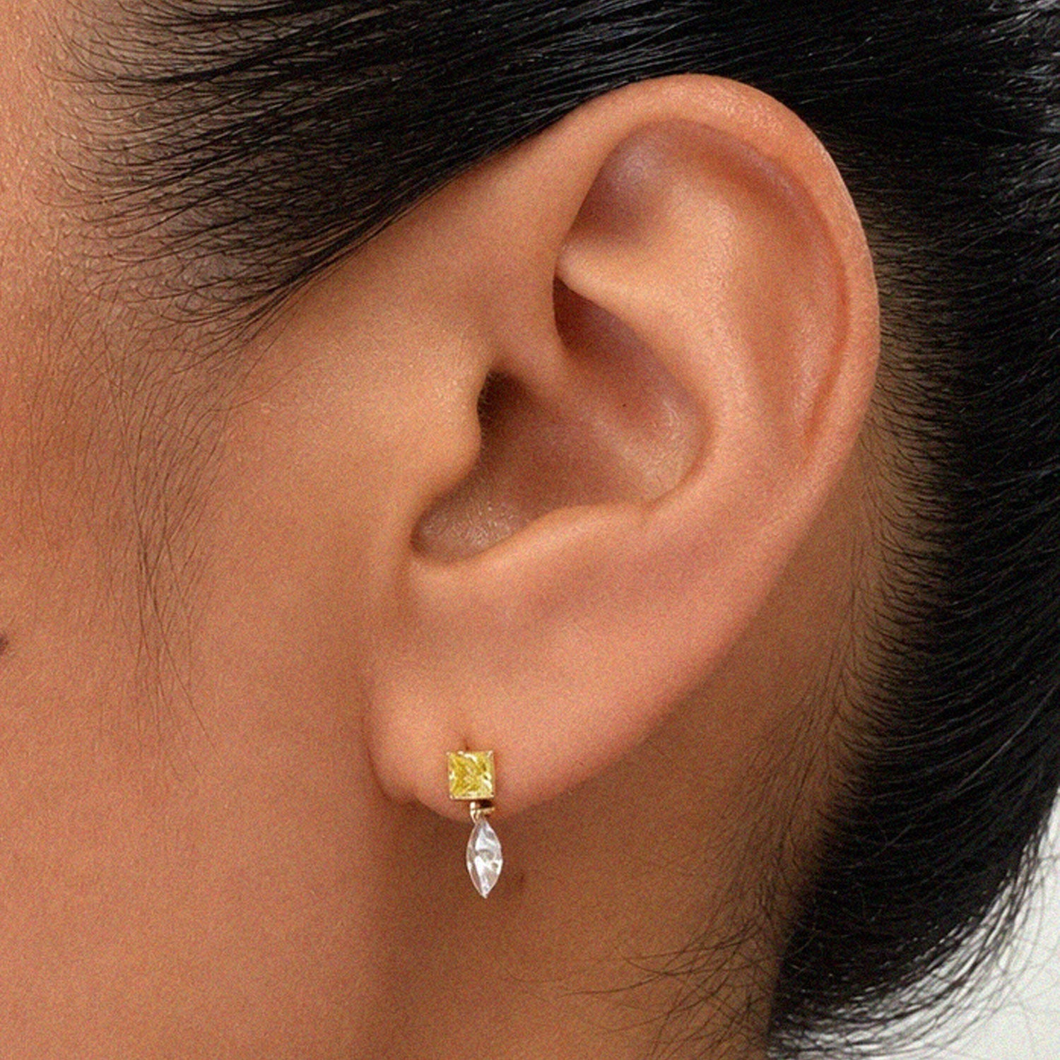 Close-up of an ear wearing a yellow gemstone stud earring with a detachable marquise-cut diamond drop charm.