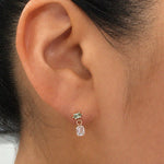Close-up of an ear wearing a pale green gemstone stud earring with a detachable emerald-cut diamond drop charm.
