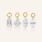 Four diamond drop charms in emerald, heart, marquise, and oval cuts, each suspended from a polished gold loop and displayed upright on a warm ivory background.