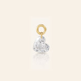 Heart-shaped diamond drop charm suspended from a polished gold loop, photographed with a subtle reflection on a warm ivory background.