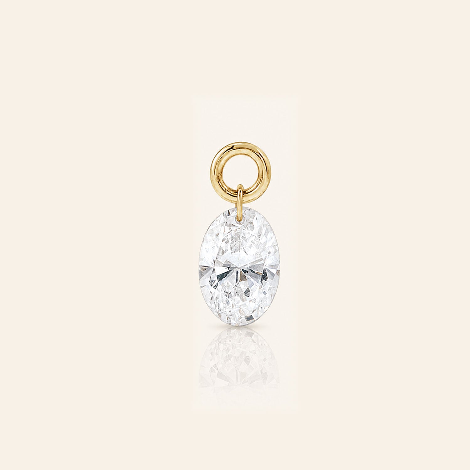 Oval-cut diamond drop charm suspended from a polished gold loop, photographed with a subtle reflection on a warm ivory background.