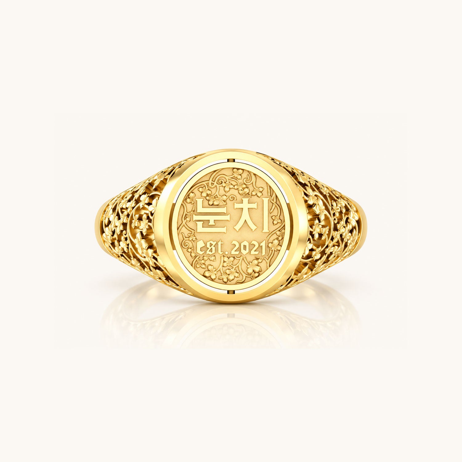 Front view of a yellow gold Reversible Dojang Ring with an ornate floral filigree band and circular face engraved with Korean Hangul and “est. 2021.”