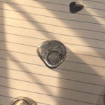 Close-up of a silver Reversible Dojang Ring impression pressed into metallic wax on lined paper, illuminated by warm sunlight and soft shadows.
