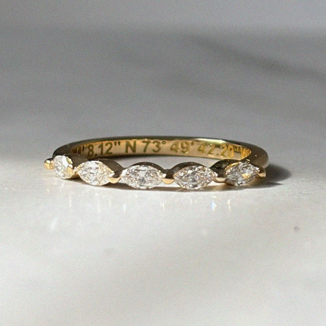 Close-up of a delicate yellow gold diamond band featuring marquise diamonds across the top half of the ring. Coordinates are engraved along the interior of the band, adding a hidden personal detail. The ring is photographed in soft natural light against a neutral background.