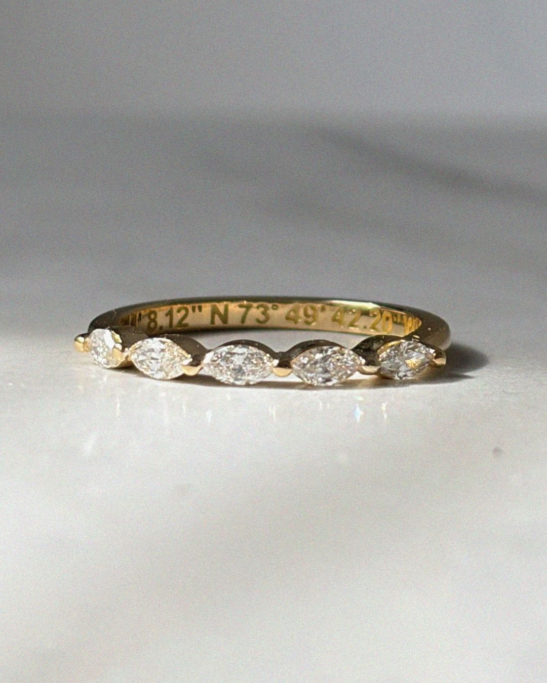 Close-up of a delicate yellow gold diamond band featuring marquise diamonds across the top half of the ring. Coordinates are engraved along the interior of the band, adding a hidden personal detail. The ring is photographed in soft natural light against a neutral background.