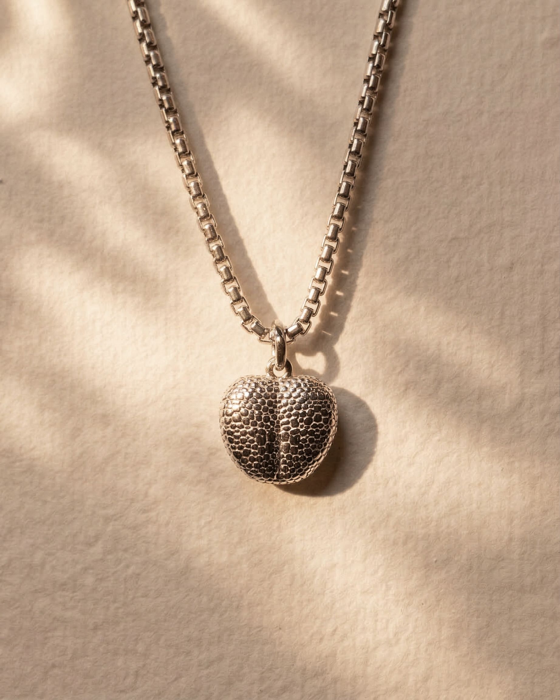 Sterling silver pendant engraved with a dog’s nose print hanging from a box chain necklace.