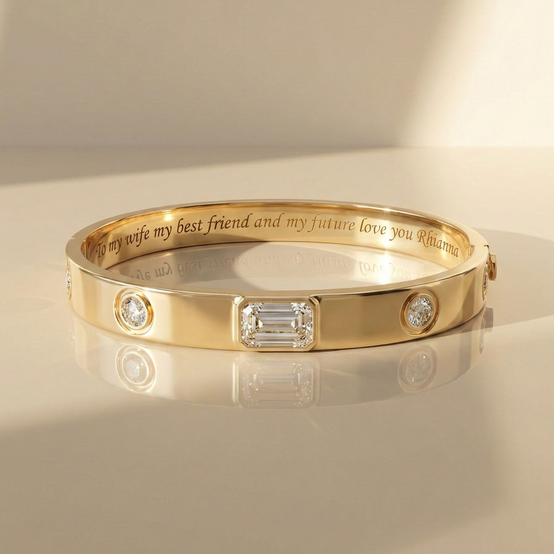 Yellow gold bangle bracelet with an emerald-cut diamond center and round diamond accents, featuring an engraved interior message.