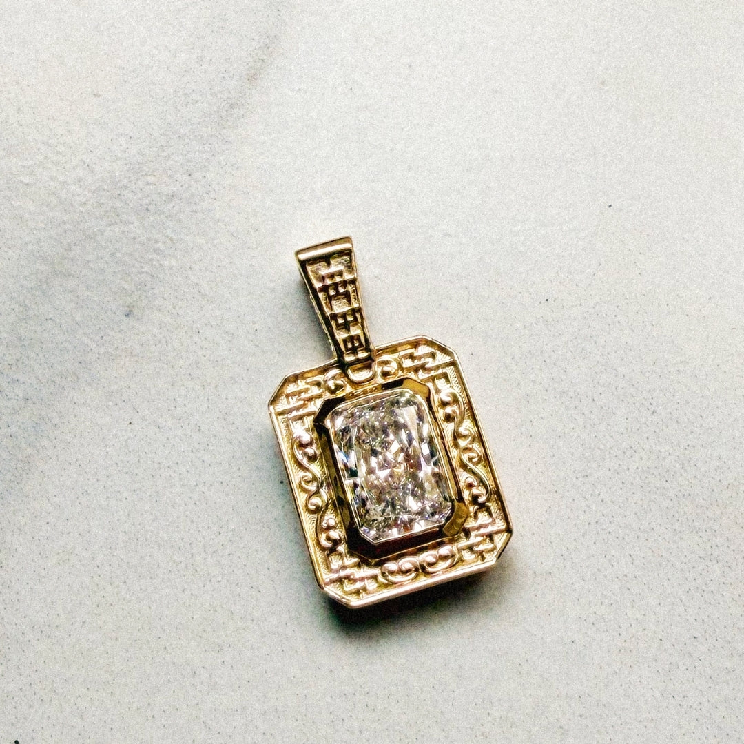 Finished rectangular gold pendant featuring a radiant-cut diamond in a bezel setting, surrounded by an ornate frame of geometric latticework and scrolling details, with matching lattice detailing on the bail.