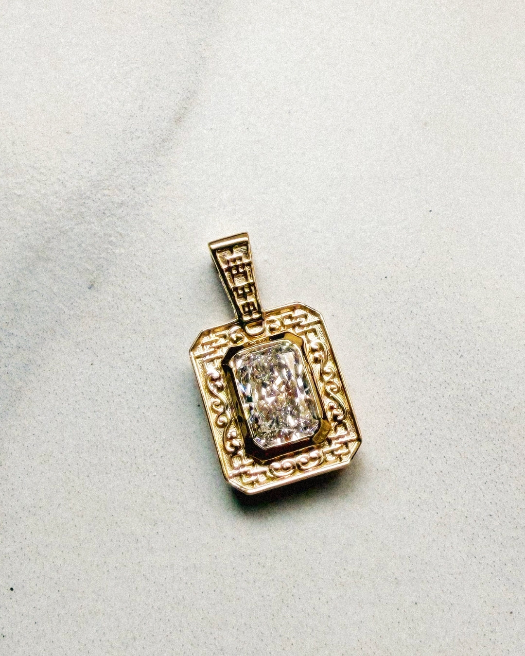 Finished rectangular gold pendant featuring a radiant-cut diamond in a bezel setting, surrounded by an ornate frame of geometric latticework and scrolling details, with matching lattice detailing on the bail.