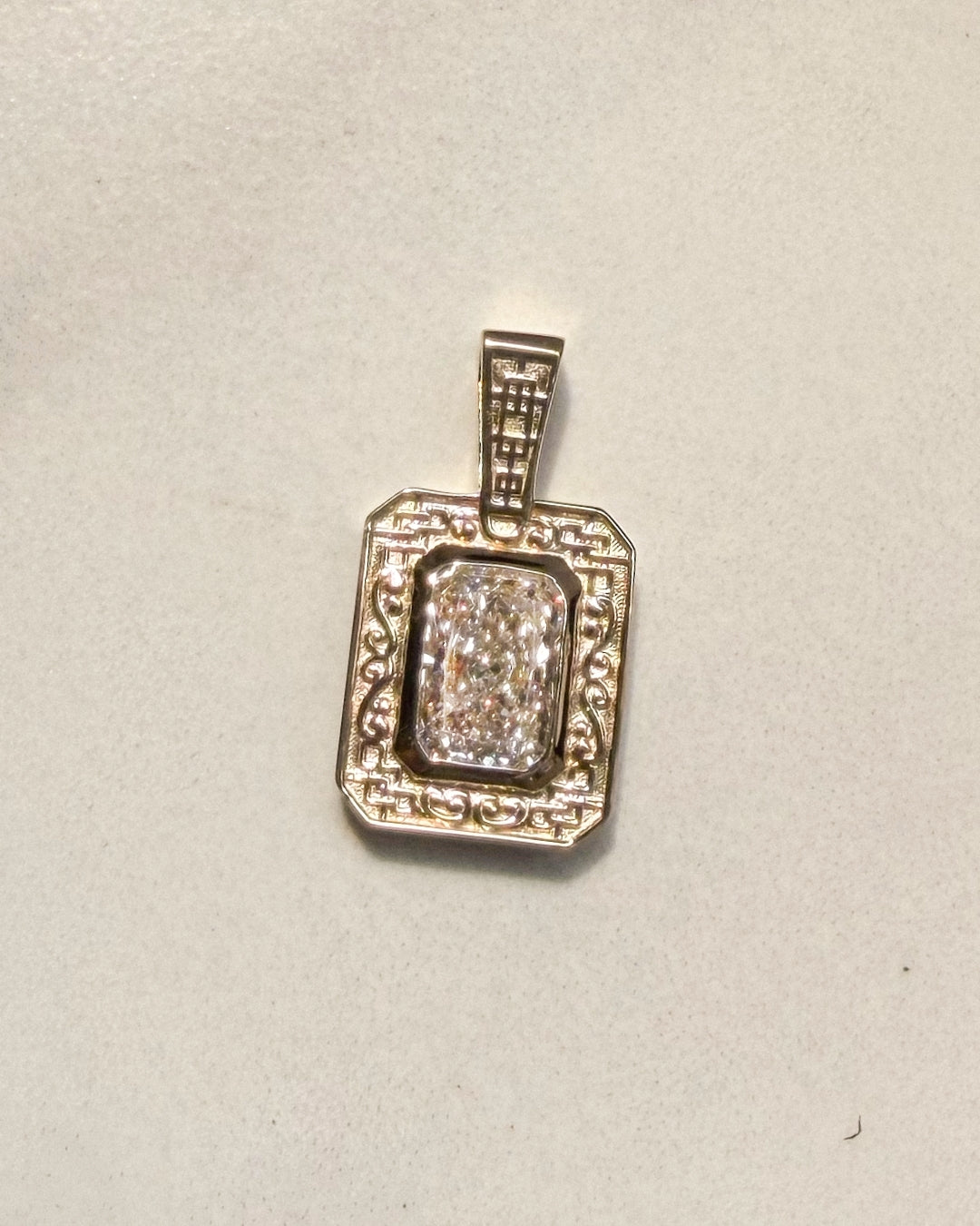 Finished rectangular gold pendant featuring a radiant-cut diamond in a bezel setting, surrounded by an ornate frame of geometric latticework and scrolling details, with matching lattice detailing on the bail.