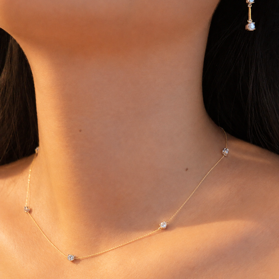 Close-up of a bride wearing a delicate oval diamond station necklace with a coordinating three-stone diamond drop earring.