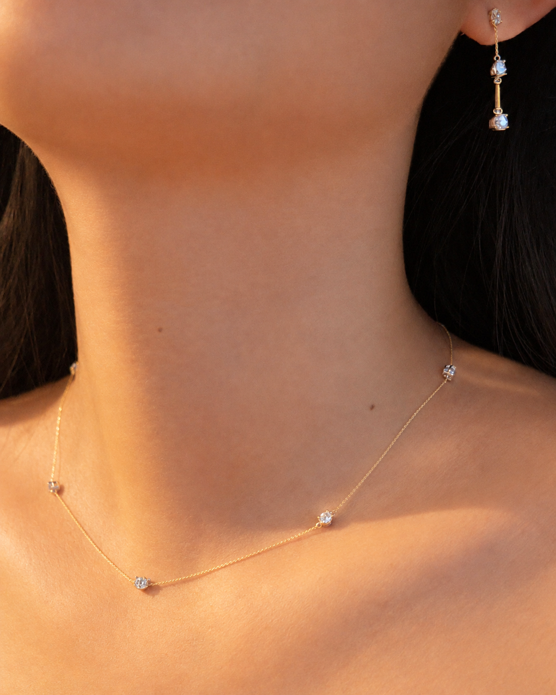 Close-up of a bride wearing a delicate oval diamond station necklace with a coordinating three-stone diamond drop earring.
