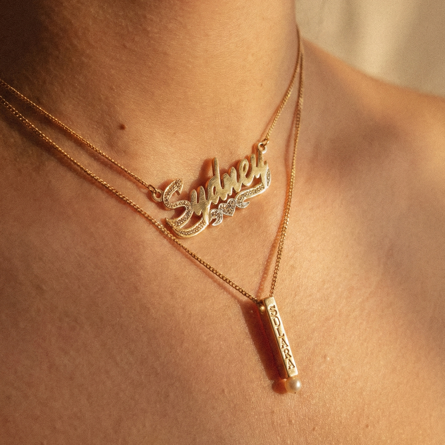Necklace with 'Sydney' nameplate pendant and a pearl bar pendant etched with SOLARA on a person's neck