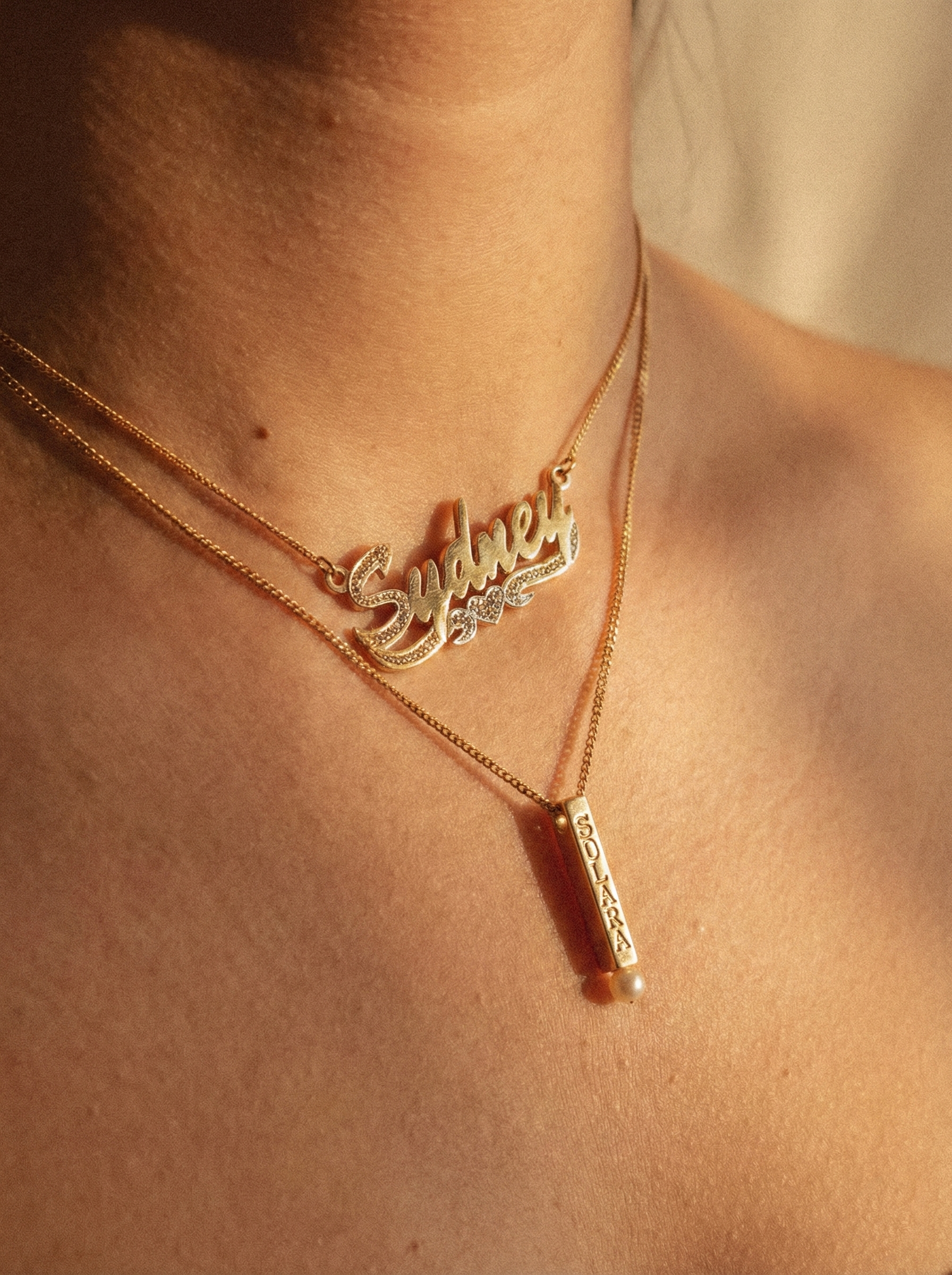 Necklace with 'Sydney' nameplate pendant and a pearl bar pendant etched with SOLARA on a person's neck