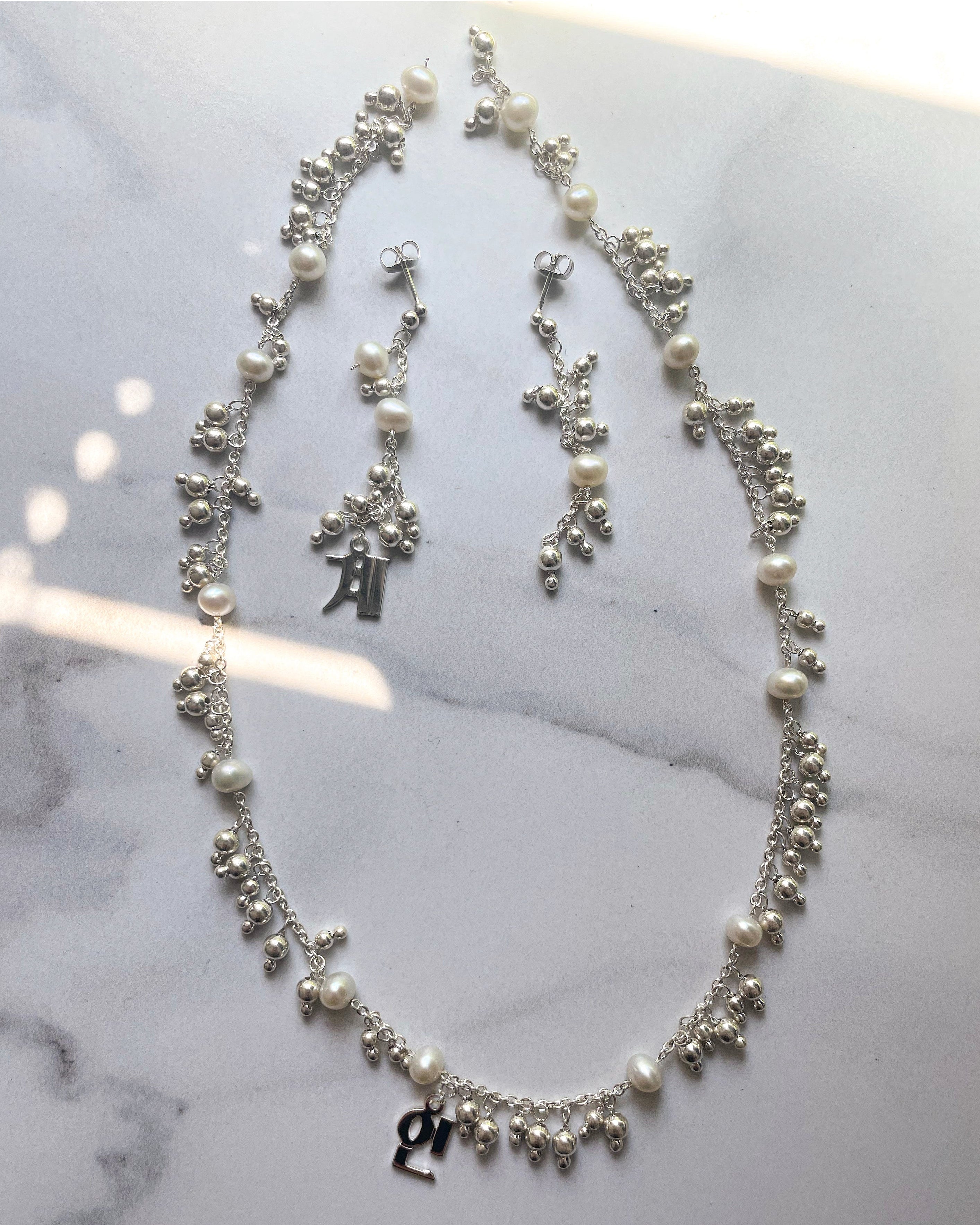 Sterling silver necklace and matching drop earrings with freshwater pearls and clustered silver bead charms, laid flat on a marble surface.