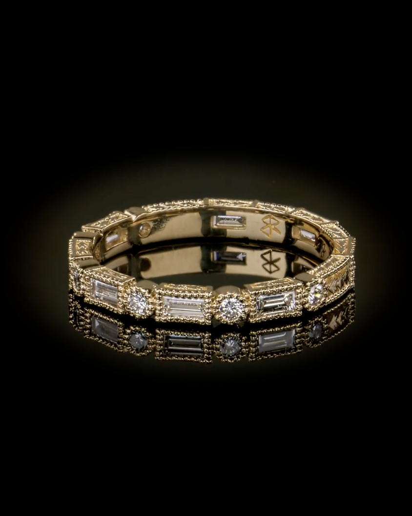 Yellow gold diamond eternity band with alternating baguette and round diamonds in milgrain settings on a black reflective surface.