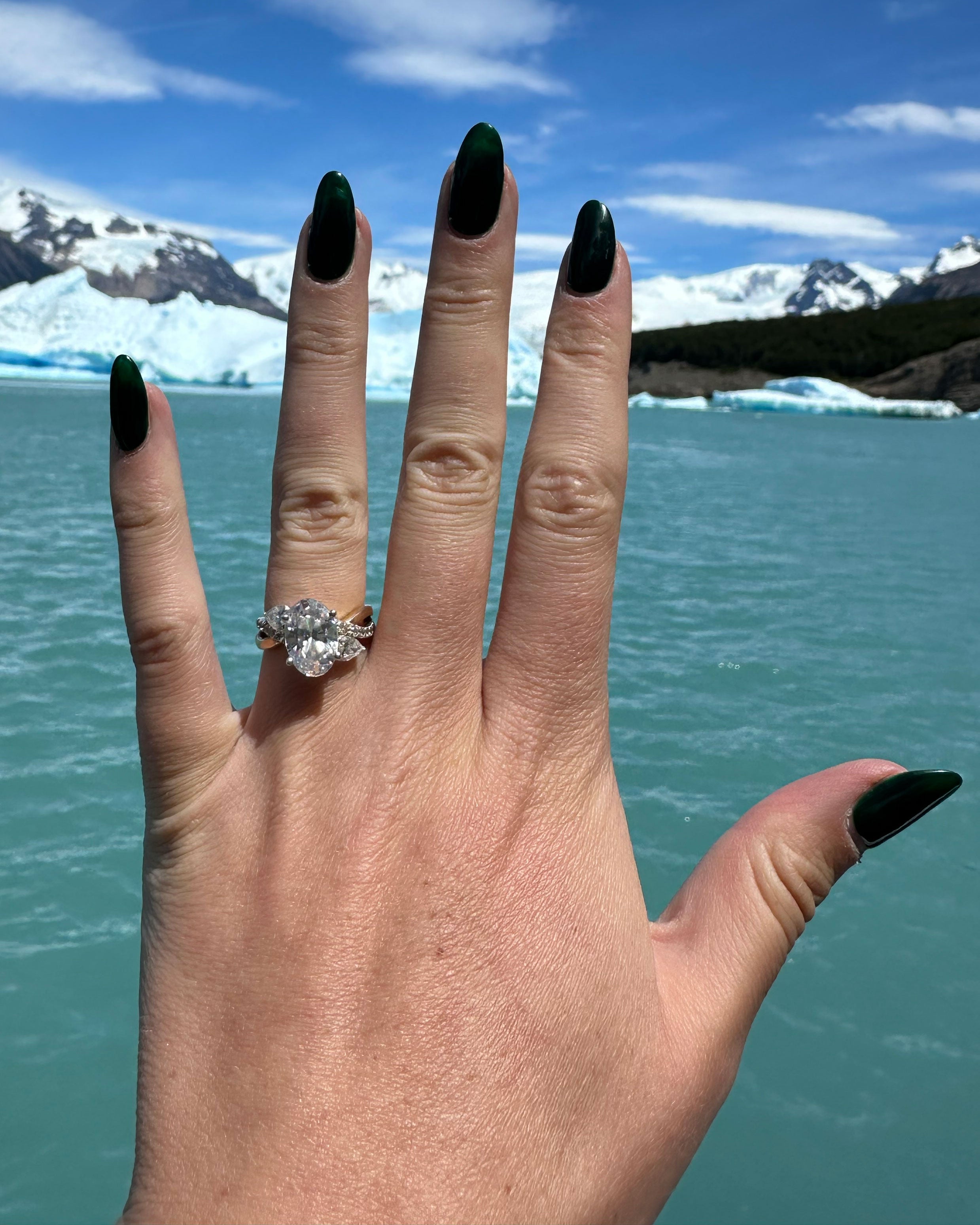 Oval diamond ring on a person's hand against a landscaper water mountain view.